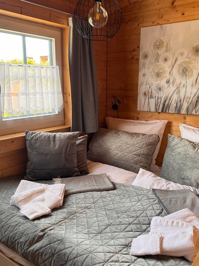Ein gemütliches Schlafzimmer mit Holzverkleidung und großen Fenstern. Das Bett ist mit grauen Kissen und frischen Handtüchern dekoriert.
