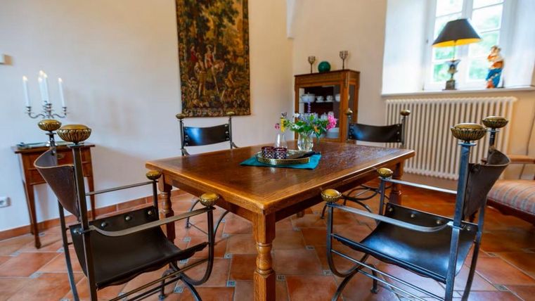 Ein einladender Essbereich mit einem Holztisch und mehreren Stühlen. Neben dem Tisch sind eine Blume und dekorative Gegenstände sichtbar.