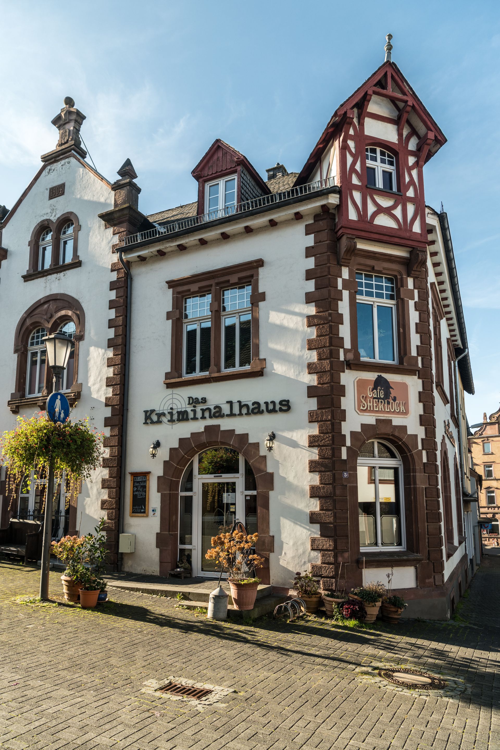 Historisches Gebäude mit Fachwerkdetails, beschriftet als 'Das Kriminalhaus' und 'Café Sherlock', bei sonnigem Wetter in Hillesheim.