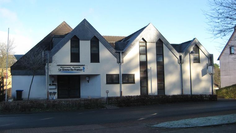 Ein modernes Gebäude mit spitzem Dach und der Aufschrift 'Ristorante Pizzeria La Sirena Da Franco' an der Fassade.