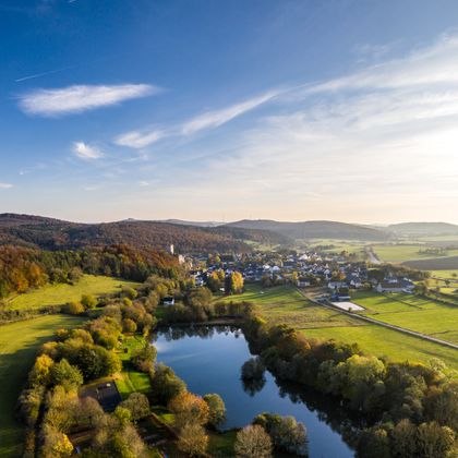 Blick auf Ort Kerpen mit angrenzendem Stausee umrandet von herbstlichen Wäldern..