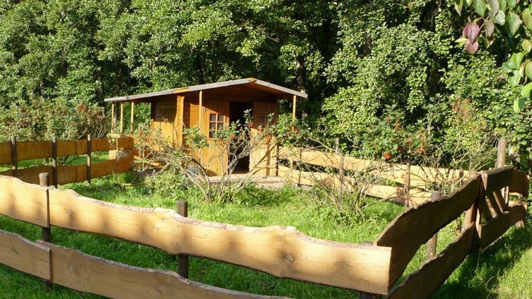 Ein gemütliches Holzhaus, umgeben von einem Holzzaun. Die grüne Wiese und die Bäume im Hintergrund schaffen eine ruhige Atmosphäre.