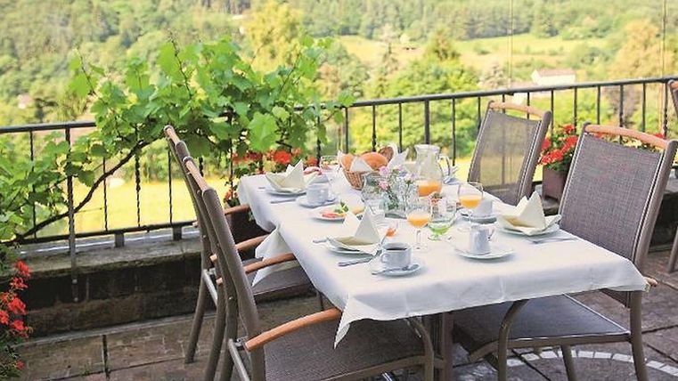 Een mooi gedekte tafel op een terras met uitzicht op een groene landschap. Op de tafel staan ontbijtgerechten en drankjes klaar.