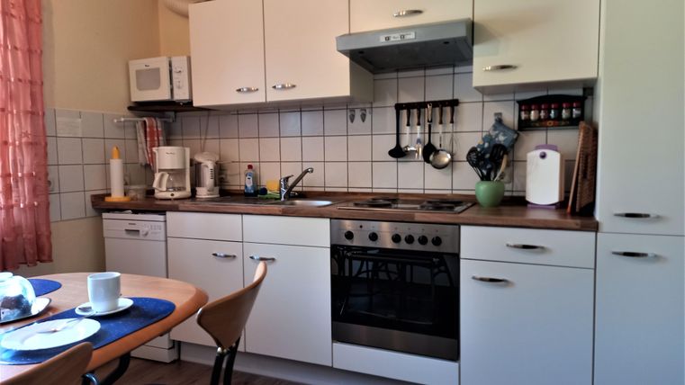 A modern kitchen with white cabinets and a wooden countertop. On the table are a cup and a plate as well as some kitchen appliances.