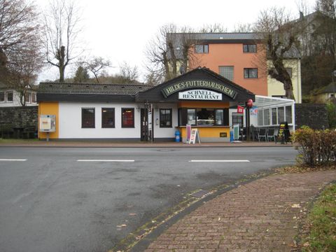 Hildes Futterhäuschen in Stadtkyll, ein Schnellrestaurant mit gelber und weißer Fassade, umgeben von kahlen Bäumen und Wohnhäusern.