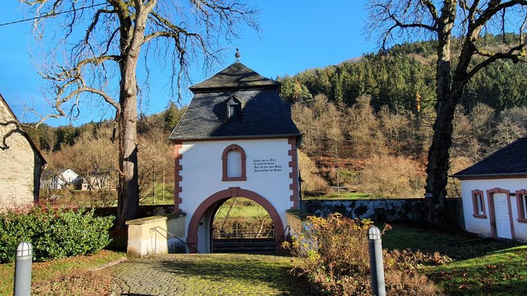 Une porte historique avec une arche, entourée d'arbres et de douces collines. Le ciel est clair et bleu.