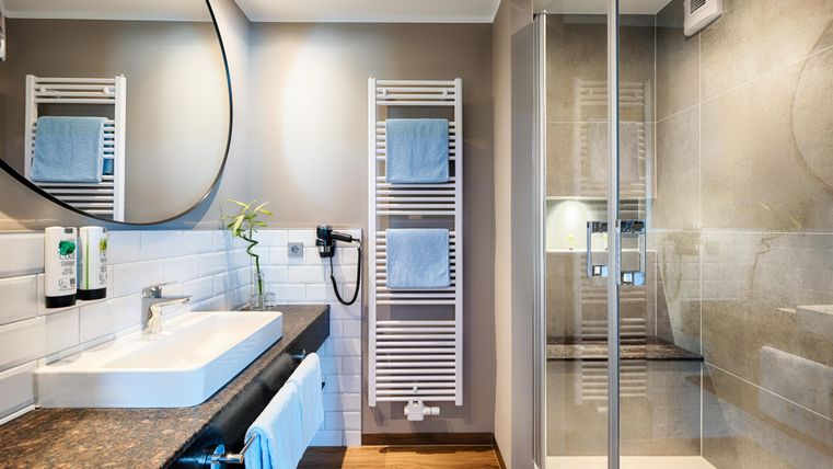 Ein modernes Badezimmer mit einer Dusche, einem großen Spiegel und einem Waschbecken. Die Wände sind in sanften Farben gehalten und es gibt Handtücher zum Aufhängen.