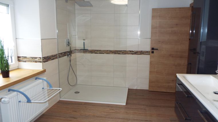 Ein modernes Badezimmer mit einer großen, begehbaren Dusche und einem Holzfußboden. Helle Fliesen und ein eleganter Waschtisch runden das Design ab.