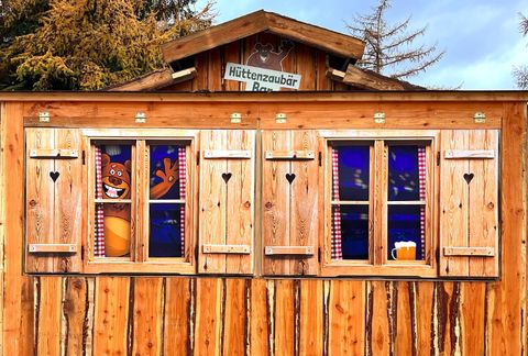 Ein gemütliches Holzhaus mit bunten Fensterläden. Im Fenster ist eine bunte Figur und ein Bierkrug zu sehen.