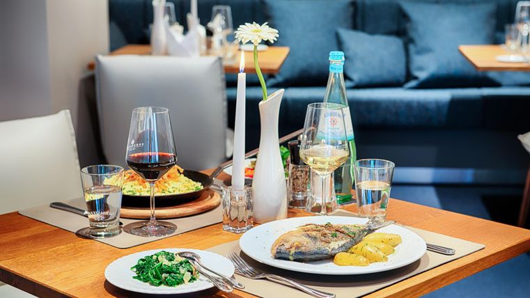 Ein Tisch in einem Restaurant mit Fischgericht, Kartoffeln, Spinat, Rot- und Weißwein, Wasserflasche und Kerze.