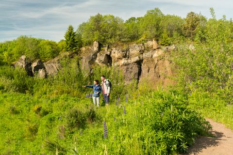 Zwei Wanderer stehen vor der felsigen Vulkanwand in einer grünen Landschaft.