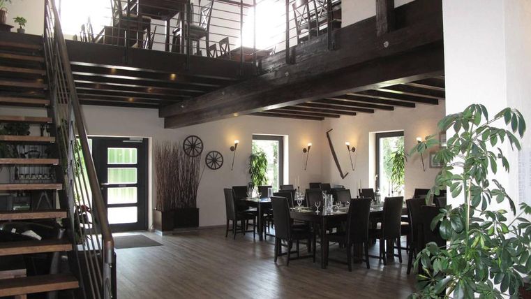 Moderne Scheune mit Holzbalken, Treppe, Esstischen und Pflanzen. Helle Fenster und stilvolle Dekoration.