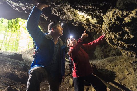 Zwei Personen mit Strinlampen erkunden die Felswände im Inneren einer Höhle.
