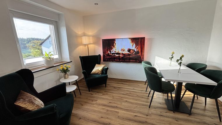 Gemütlicher Caféraum mit unterschiedlich großen Tischen und gemütlichen Stühlen neben einem großen Fenster.