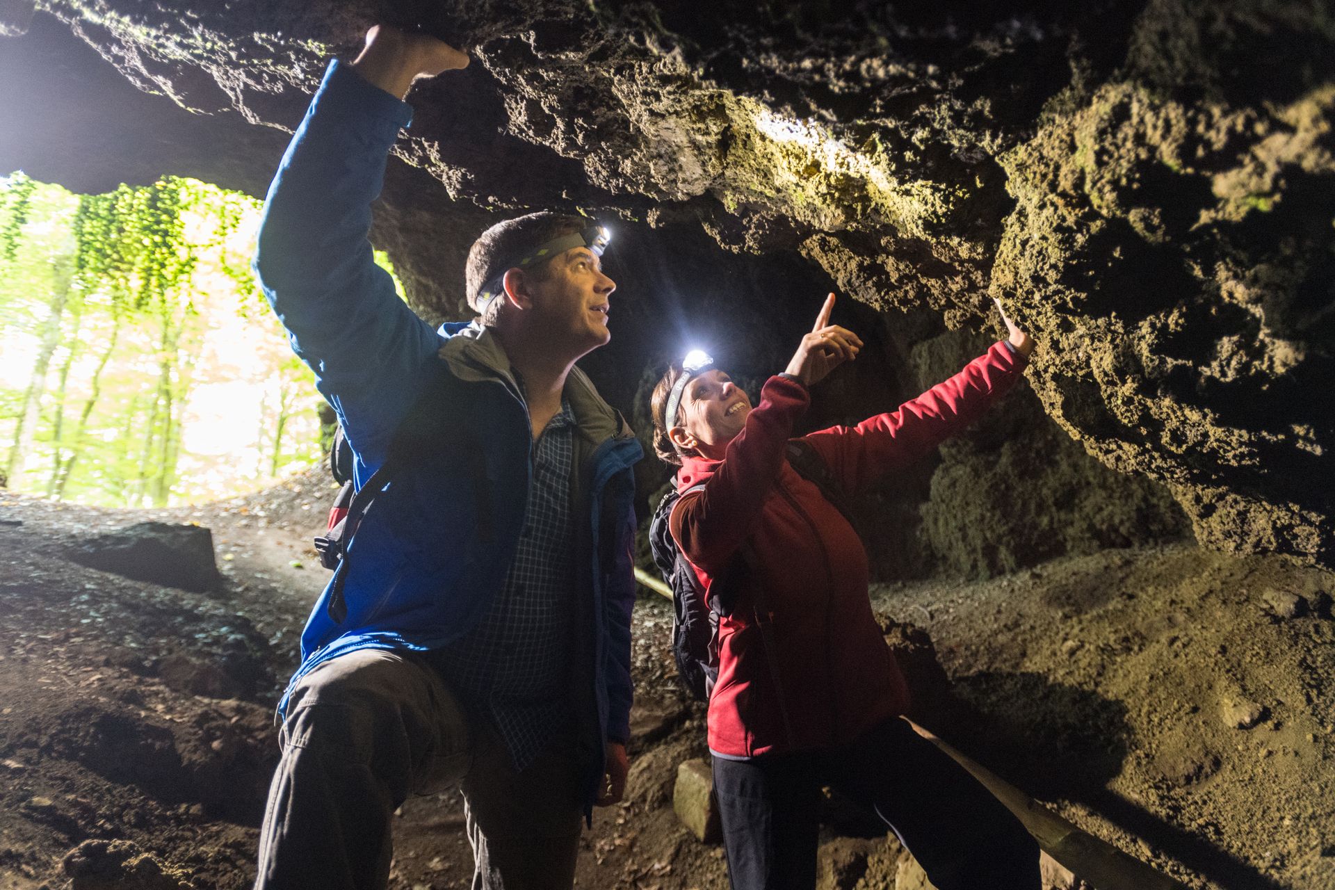Zwei Personen mit Stirnlampen erkunden die Steinwände einer Höhle.