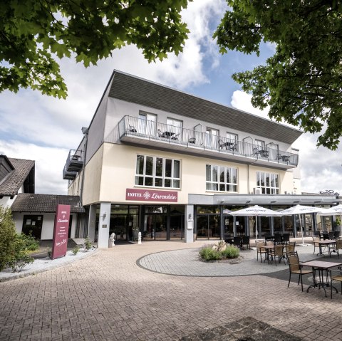 Au&szlig;fasse des Hotel L&ouml;wenstein in Gerolstein mit mehreren Tischen und St&uuml;hlen im Au&szlig;enbereich.