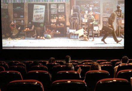 Rows of seats in a cinema auditorium photographed from behind, with several guests sitting and watching the screen. A cartoon film is showing on the cinema screen.