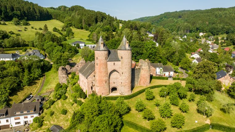 Luchtfoto van Kasteel Bertrada in Mürlenbach, omgeven door groen landschap en huizen.