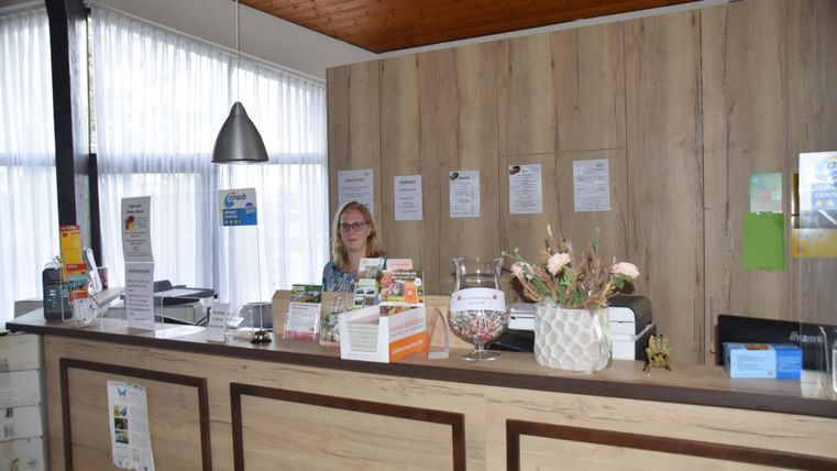 Rezeption eines Waldferienparks mit einer Frau hinter dem Tresen, umgeben von Broschüren und Dekorationen.