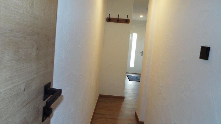 Ein heller Flur mit Holzfußboden und einer weißen Wand. An der Wand hängen Haken für Kleidung.