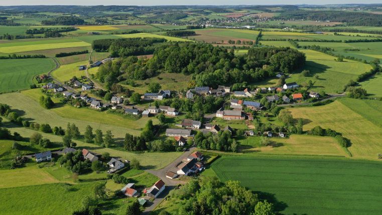Eine malerische Landschaft mit einem kleinen Dorf, umgeben von grünen Feldern und Bäumen. Die Weite der Natur vermittelt Ruhe und Idylle.