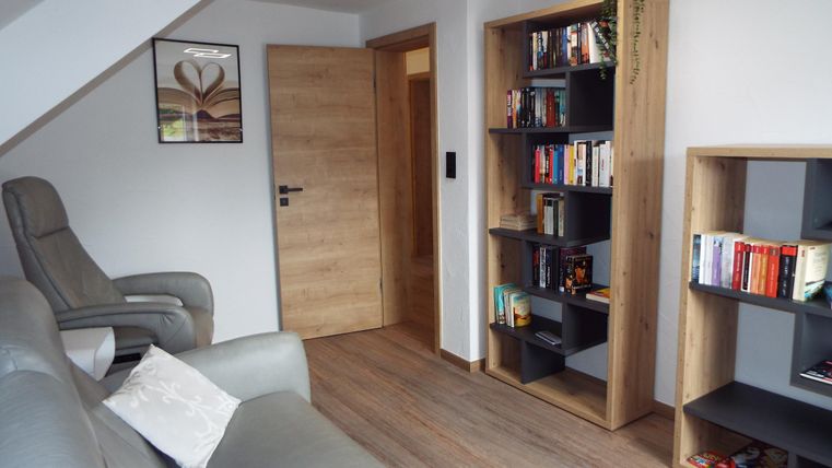 Ein gemütliches Wohnzimmer mit einem bequemen Sessel und einem Bücherregal. Der Raum hat einen modernen Stil und ist gut beleuchtet.