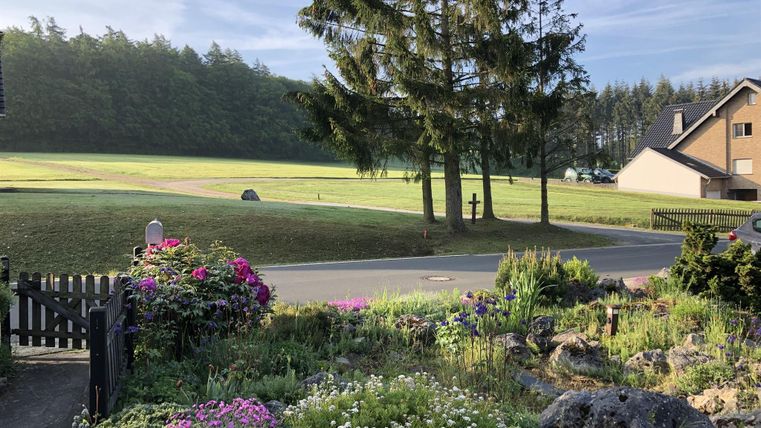 Een mooie tuin met kleurrijke bloemen en een verzorgde hekwerk. Op de achtergrond is een groene wei en een huis te zien.