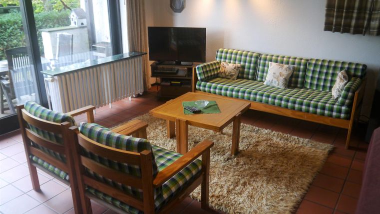 Ein gemütliches Wohnzimmer mit einer karierten Couch und zwei passenden Stühlen. Es gibt einen Couchtisch und große Fenster, die Licht hereinlassen.