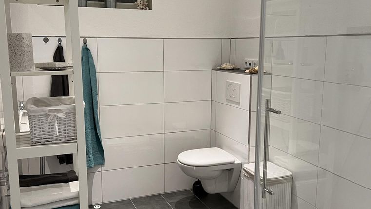 Een moderne badkamer met een heldere douchewand en tegelvloer. Het heeft lichte muren en een schone, nette inrichting.