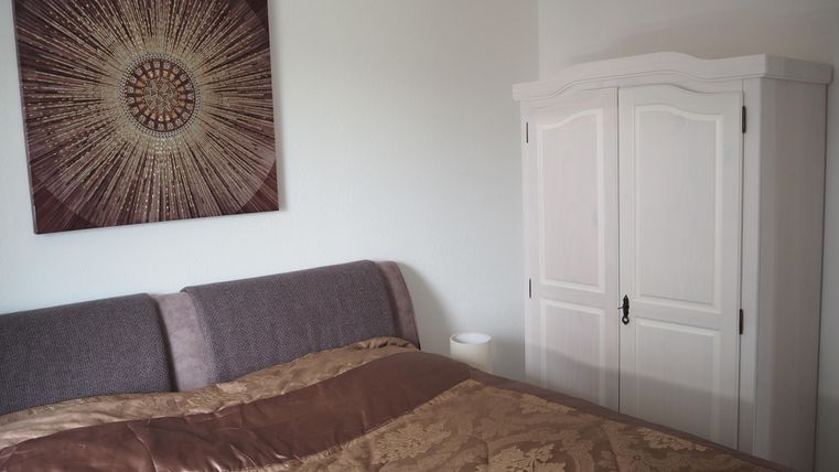 Ein gemütliches Schlafzimmer mit einem großen Bett und einer goldenen Bettdecke. An der Wand hängt ein dekoratives Bild, und neben dem Bett steht ein weißer Schrank.