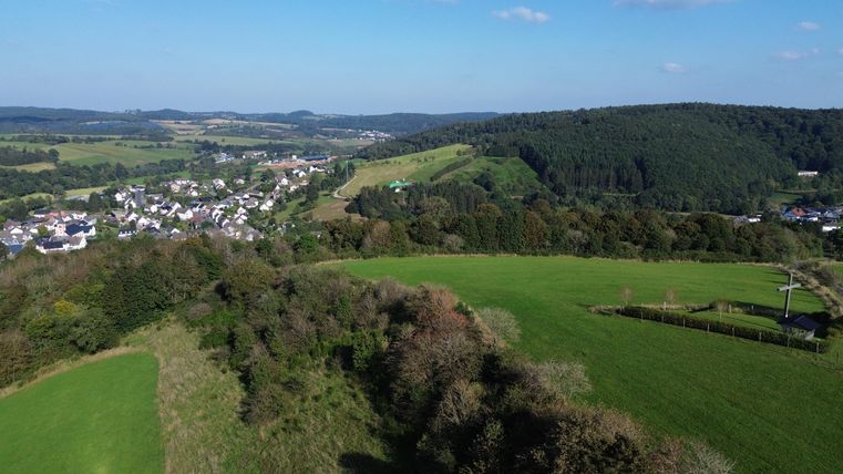 Blick von oben auf weite Wiesen- und Waldlandschaft mit dazwischenliegendem Dorf Stadtkyll im Tal.