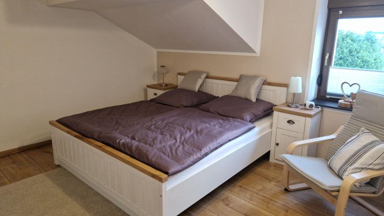 Ein gemütliches Schlafzimmer mit einem Doppelbett und zwei Kissen. Neben dem Bett steht ein Sessel und ein Nachttisch mit einer Lampe.