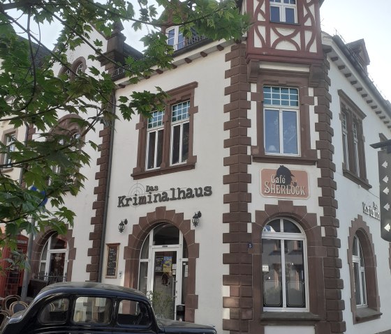 Ein historisches Geb&auml;ude mit der Aufschrift 'Das Kriminalhaus' und 'Caf&eacute; Sherlock'. Vor dem Geb&auml;ude steht ein schwarzes Oldtimer-Auto., &copy; Albert Junk