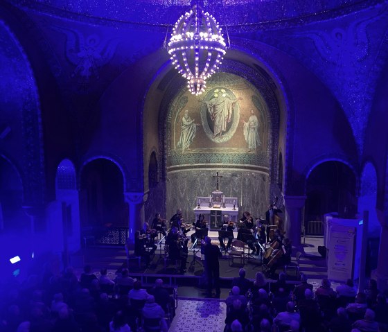Schwach beleuchteter Innenraum der Erl&ouml;serkirche Gerolstein. Im Altarraum Musikanten und ein gro&szlig;es Publikum in den Sitzb&auml;nken.