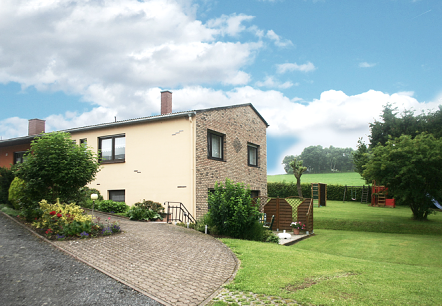 Courtyard entrance to a residential house with some trees and bushes at the house and a large meadow next to it.