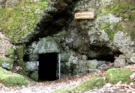 Een met mos bedekte rots met een donkere grotingang, met het opschrift 'Schwedenfeste'. Herfstbladeren bedekken de grond., &copy; Touristik GmbH Gerolsteiner Land
