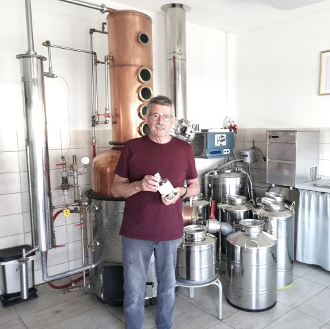 Ein Mann vor einer Destilliermaschine mit einer Flasche Gin in der Hand.