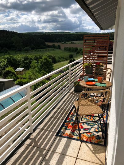 Ein schöner Balkon mit Blick auf die grüne Landschaft. Ein Tisch und zwei Stühle sind dekorativ eingerichtet.