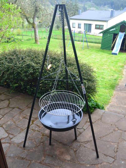 Een mobiele grill staat op een bestrate vloer. Op de achtergrond zijn groene weiden en een speeltuin zichtbaar.