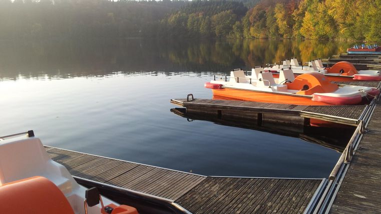 Un lac paisible avec des bateaux au quai. En arrière-plan, on voit des arbres colorés qui soulignent la beauté de la nature.