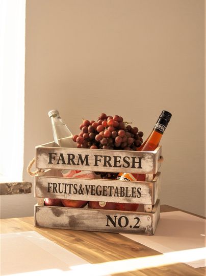 Eine dekorative Kiste mit frischen Früchten und Gemüse. Darin befinden sich Trauben und Flaschen mit Getränken.