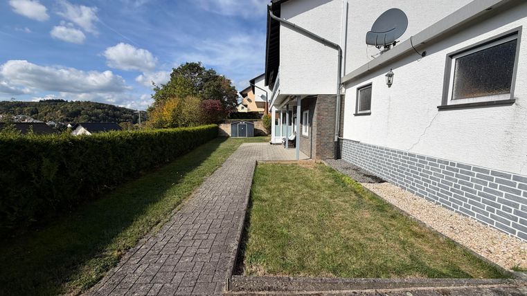 Un chemin bien entretenu mène à un bâtiment moderne avec un jardin vert. Le ciel est bleu avec quelques nuages.
