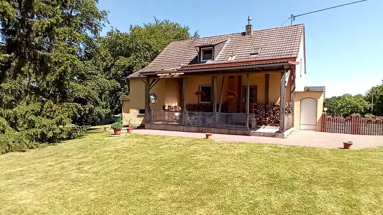 Ein gemütliches Haus mit einem großen Garten und viel grünem Rasen. Der Raum ist von Bäumen umgeben und hat eine sonnige Terrasse.