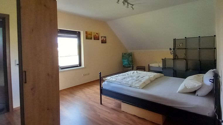 Schlafzimmer in freundlich gehaltenen Wandfarben mit zwei Einzelbetten, getrennt durch ein Raumteiler-Regal,  Kleiderschrank mit Spiegeltür, Zugang zu Balkon West