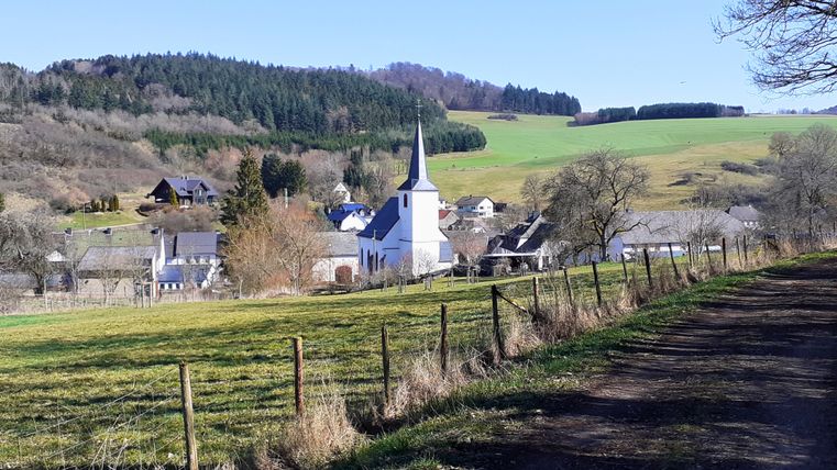 Landschaft mit Dorf, Kirche und Hügeln im Hintergrund.