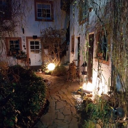 Een gezellige binnenplaats met een geplaveide weg en zachte verlichting. Omgeven door planten en oude gebouwen straalt het een ontspannen sfeer uit.