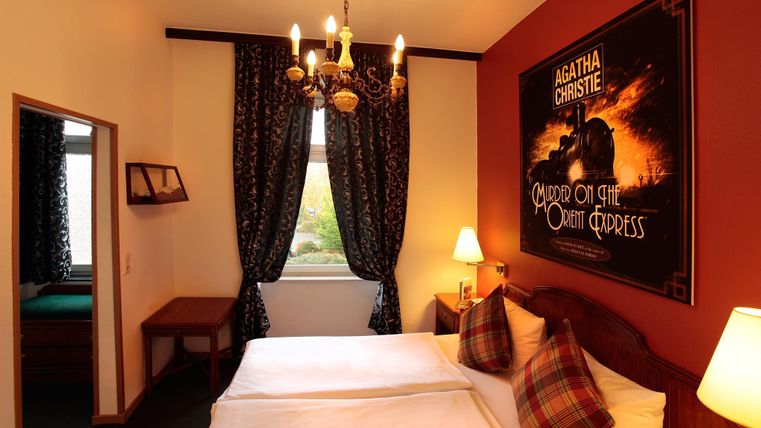 Une chambre d'hôtel confortable avec deux lits et un décor élégant. Un grand poster d'Agatha Christie est accroché au mur.