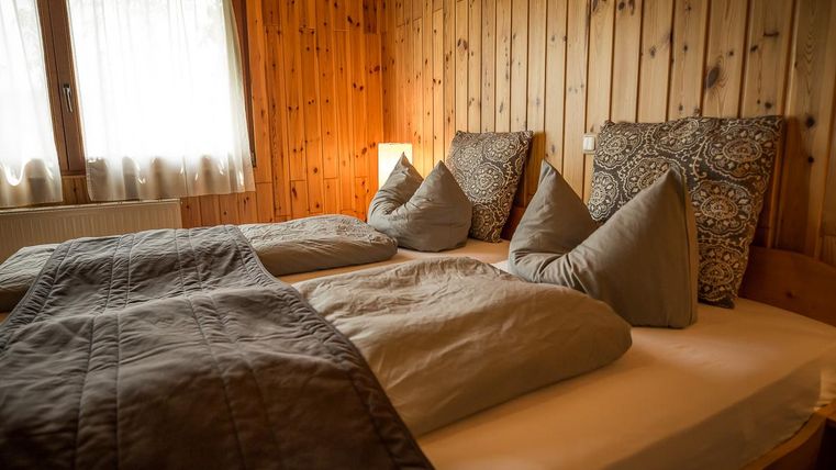 Ein gemütliches Schlafzimmer mit Holzwänden und zwei Betten. Die Kissen sind stilvoll angeordnet und das Licht ist sanft.