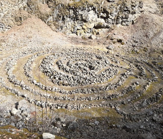 A spiral-shaped stone circle in a rocky environment, surrounded by moss and dry foliage., © Touristik GmbH Gerolsteiner Land, Ute Klinkhammer
