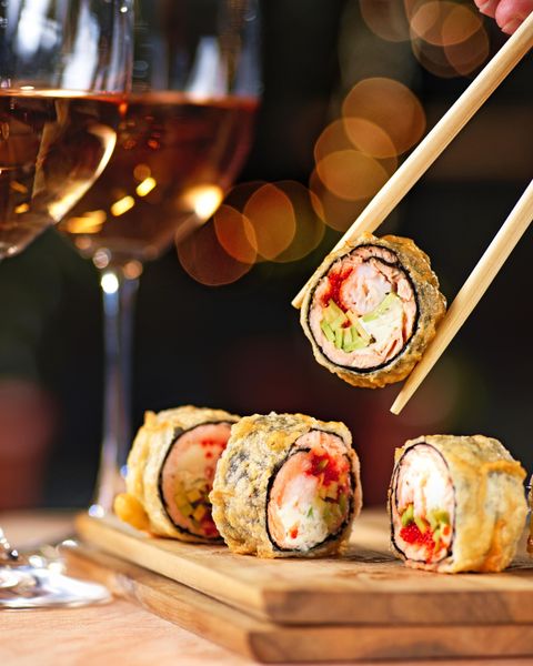 Nahaufnahme von frittiertem Sushi auf einem Holzbrett mit einem Glas Wein im Hintergrund.